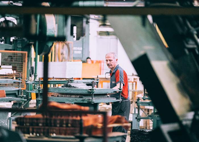 A worker in a striped shirt operates machinery in an industrial setting, possibly considering a workers compensation lawsuit. Various machines and equipment are visible around the worker, creating a busy and productive atmosphere within the factory or manufacturing plant.